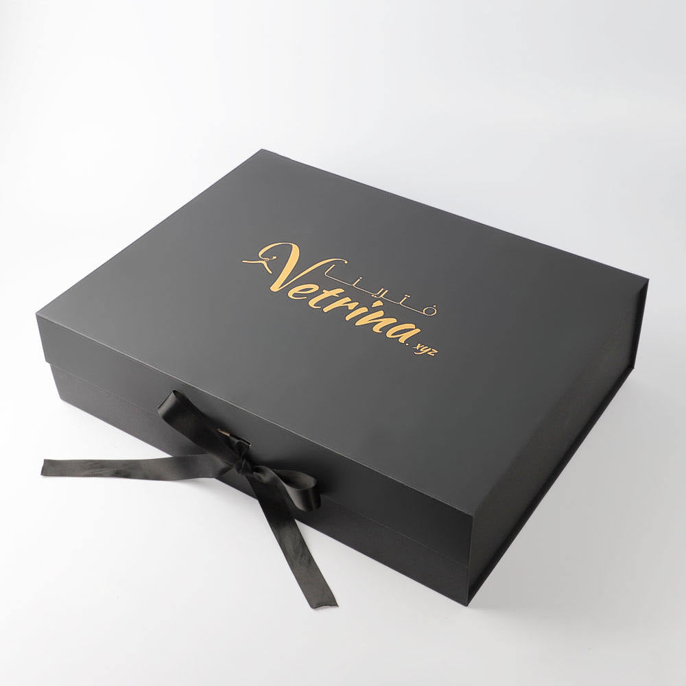 Closed black custom gift box with gold logo detail and a black ribbon tied at the front.