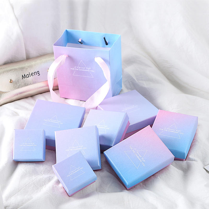 Pastel blue and pink gradient jewelry boxes arranged with a matching handled paper gift bag.